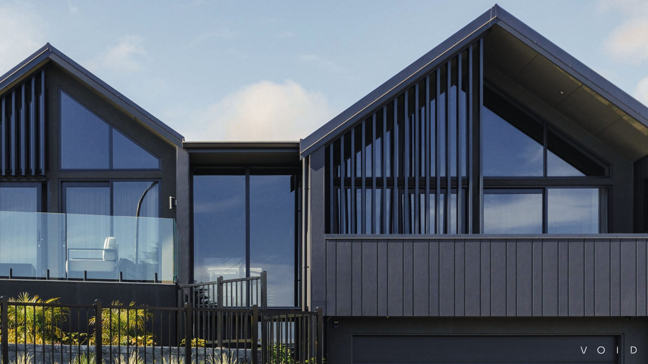 Black house exterior with dual gables, large windows, and vertical panelling. VOID Architects New Plymouth