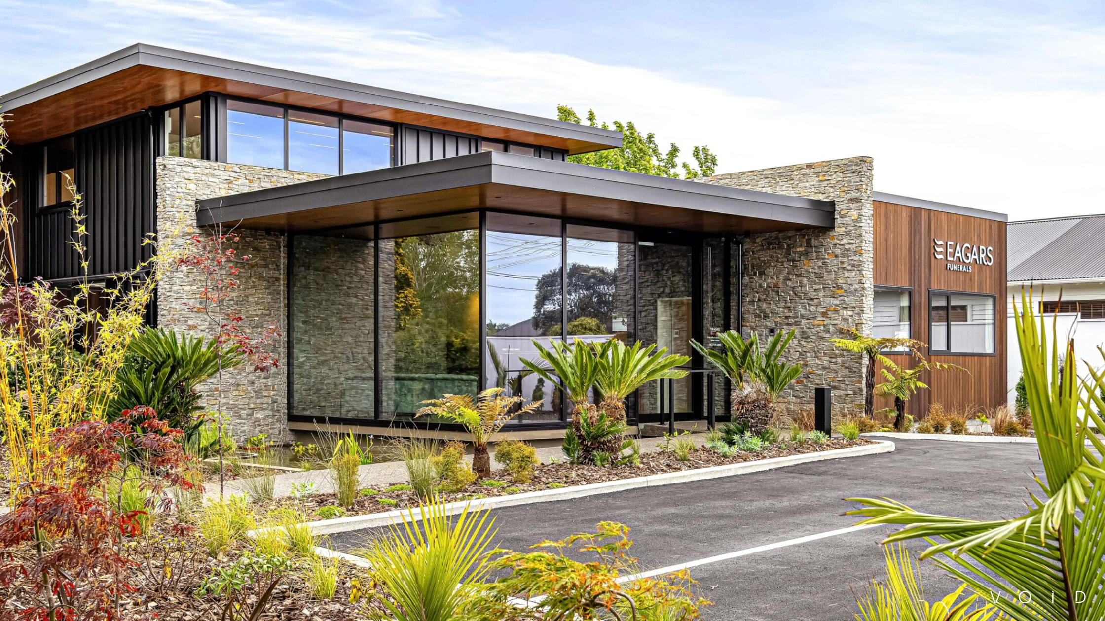 Exterior of a stone building with large windows and layered landscaping | VOID Architects New Plymouth