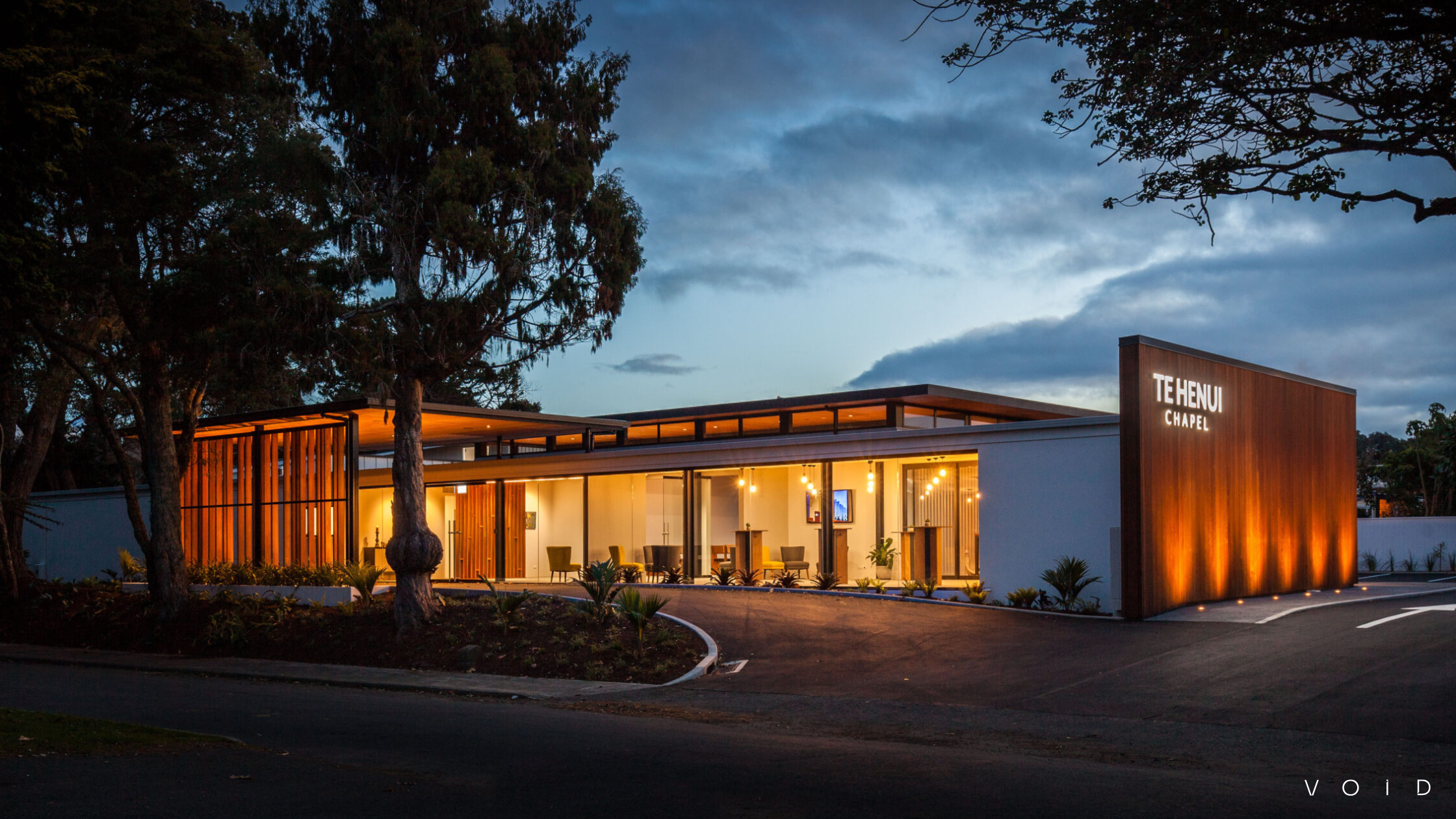 A building exterior wide angle with warm interior lighting, large windows, accent lights, and Te Henui Chapel signage on the wall. 